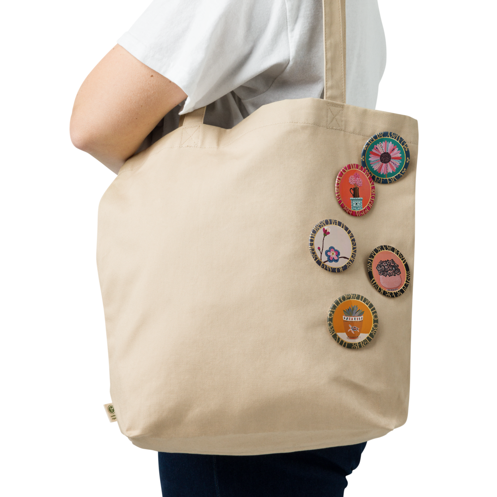 Beige tote bag with colorful patches held by a person the pins are from the Five-piece floral medallion art pin set including daisy hydrangea plum blossom rose bouquet and potted succulent pinback buttons by Szeto on a white background