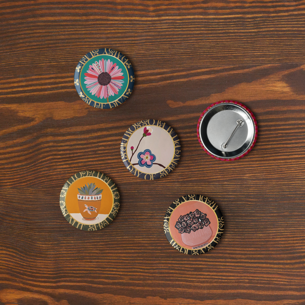 Five decorative bottle caps with floral designs on a wooden surface from the Five-piece floral medallion art pin set including daisy hydrangea plum blossom rose bouquet and potted succulent pinback buttons by Szeto on a white background